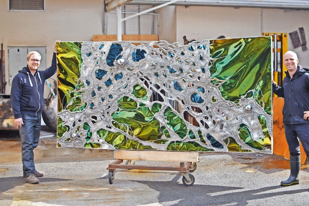 © Gahr
Robert (links) und Stefan Gahr (rechts) mit der in Grün und Blau polierten Wandplastik aus Edelstahl. Das große Wandbild "Im Fokus" wurde aus rostigem Corten-Stahl mit spiegelpoliertem Edelstahl gefertigt.
Gahr Objektkunst
