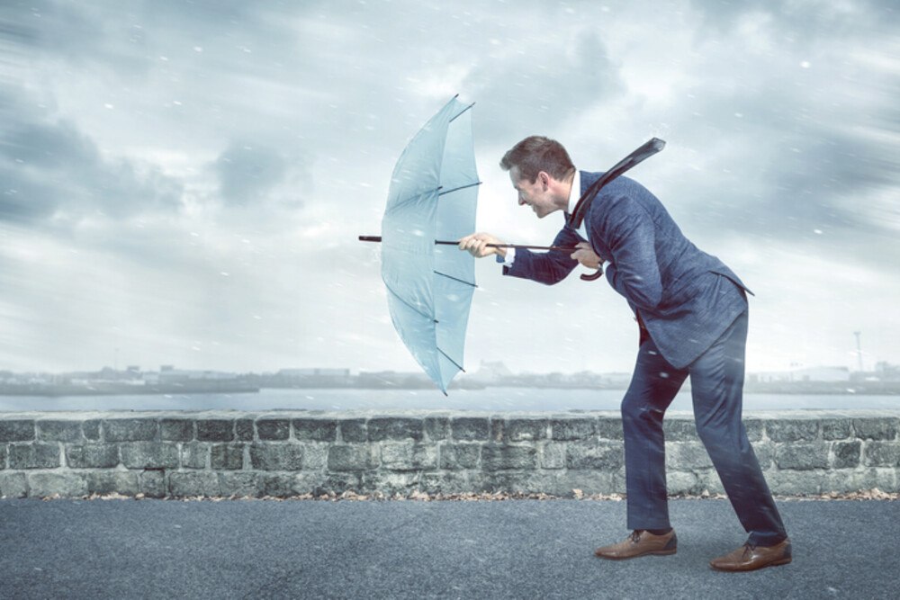 © photoschmidt iStock / Getty Images Plus Geschäftsmann mit Regenschirm im Gegenwind