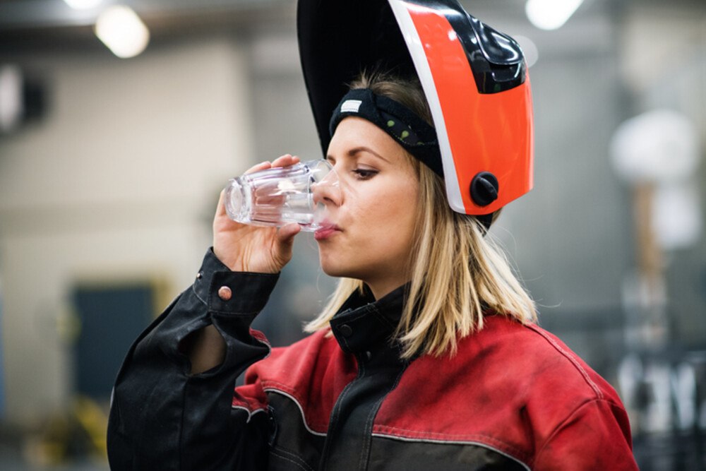 © Halfpoint iStock Gettyimages Plus Frau in Arbeitskleidung trinkt aus einem Wasserglas