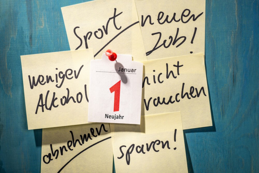© iStock / Getty Images Plus / gopixa
Der Jahreswechsel ist traditionell die Zeit der guten Vorsätze: Vielleicht das Rauchen aufgeben, mehr Sport treiben oder einfach nur weniger Süßes essen, sind einige der Klassiker.
 Das Kalenderblatt des ersten Januars ist auf eine blaue Wand aufgepinnt. Rundherum hängen Post-its mit Neujahrsvorsätzen.