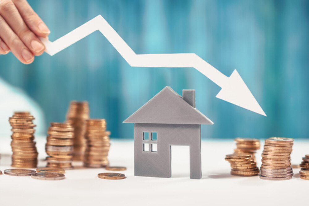 © LeManna iStock Getty Images Plus ein Pfeil, der nach unten zeigt, über einem Holzhaus neben Geldmünzen