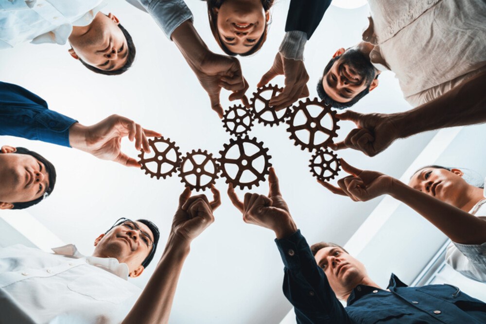 © NanoStockk iStock Getty Images Plus ein Team hält Zahnräder als Symbol