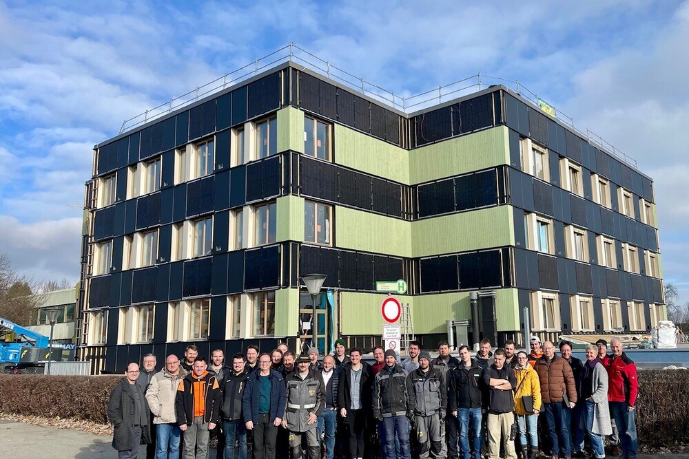 © AEE INTEC / Cornelia Ninaus
Aktuell werden am Pilotgebäude in Knittelfeld umfassende Sanierungsarbeiten durchgeführt.
Eine Gruppe an Menschen steht vor einem grün-schwarzen Gebäude.