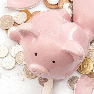 © Getty Images/Moussa81 Kaputtes, rosafarbenes Sparschwein um das herum Münzen liegen.