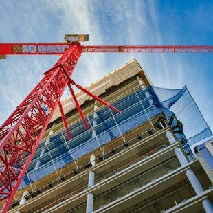 © JARAMA / iStock / Getty Images Plus via Getty Images Blick von unten auf einen Neubau mit rotem Kran im Vordergrund.
