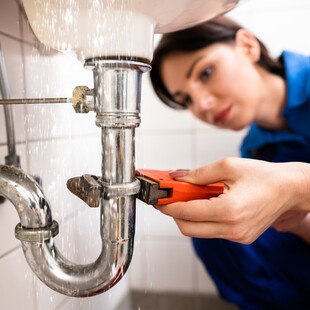 © AndreyPopov iStock Getty Images Plus Klempnerin repariert Rohr beim Waschbecken