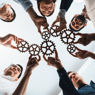 © NanoStockk iStock Getty Images Plus ein Team hält Zahnräder als Symbol